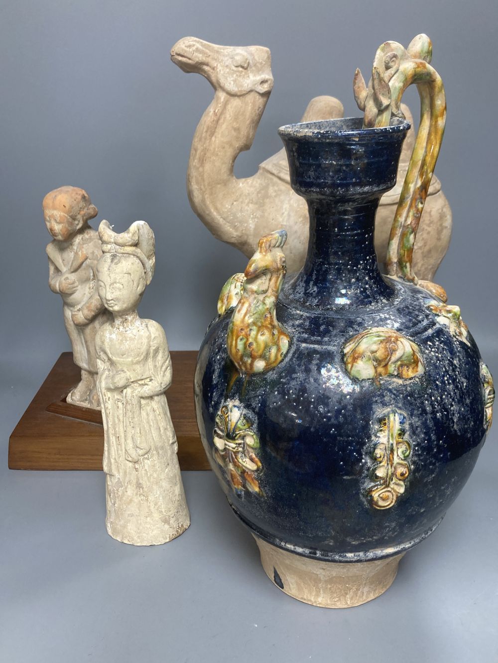A group of Chinese Tang style pottery figures, tallest 28cm and a partially glazed ewer in sancai colours against a blue ground, 40cm